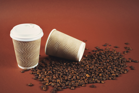 Two paper coffee cups with white covers and scattered coffee beans on brown background with copy space for text. Morning concept.の写真素材