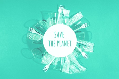 White plastic forks, transparent bags and cups with round frame on pastel turquoise background. Concept of saving the planet and environment. Flat lay minimalistic style.の写真素材