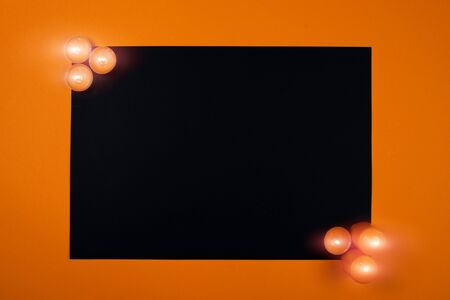 Festive black and orange background as a frame with glowing candles with fire. Copy space for text. Halloween and holly saints concept.の写真素材