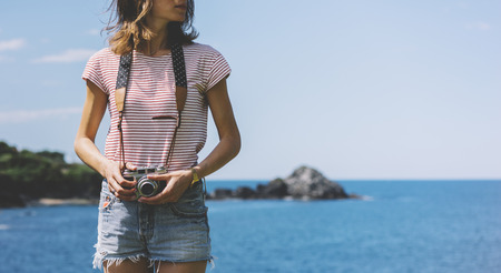 Tourist traveler photographer making pictures seascape on vintage photo camera on background yacht and boat piar, hipster girl enjoying peak mountain and nature holiday, mockup ocean waves view, blurred backdropの写真素材