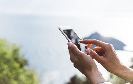 Hipster girl texting message on smartphone mobile close up, view tourist hands using gadget phone on device on background perspective mountains and sky landscape; finger touch screen cellphone mockupの写真素材