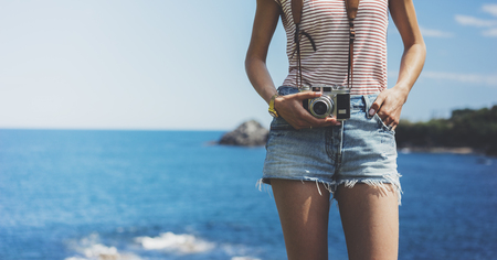 Tourist traveler photographer making pictures seascape on vintage photo camera on background yacht and boat piar, hipster girl enjoying peak mountain and nature holiday, mockup ocean waves view, blurred backdropの写真素材