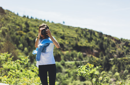 Tourist traveler photographer taking pictures of amazing landscape on vintage photo camera on background valley view mockup sun flare, hipster girl enjoying peak of foggy mountain, nature holiday conceptの写真素材