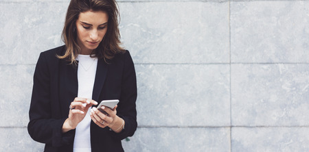 Portrait young businesswomen in black suit using smartphone isolated on background concrete gray wall mockup, pretty hipster manager holding mobile gadget, girl smiletexting message, connectの写真素材