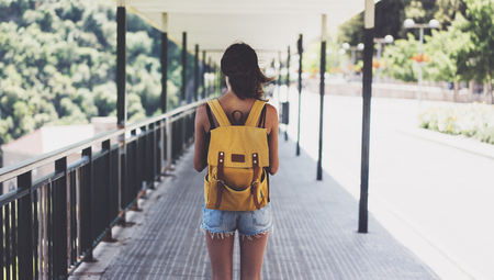 Hipster young girl with backpack enjoying summer mountain. View from a back tourist traveler in...
