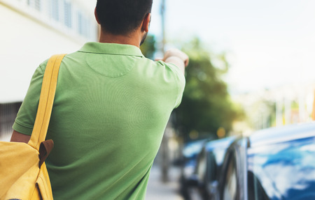 Hipster young man with backpack and map. View from back tourist traveler planning route on background sun city and pointing hand route. Person hiker visiting the sights on backdrop summer street, mockupの写真素材