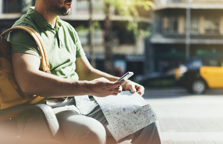 Man with yellow backpack holding smartphone, tourist looking map city on background taxi, hipster planning route using in hands mobile phone, traveler connect wifi internet, backdrop summer street, mockupの写真素材