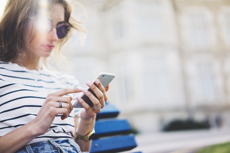 Hipster texting message on smartphone or technology, mockup of blank screen. Girl using cellphone on building castle background close. Tourist female hands holding gadget on blurred summer backdropの写真素材