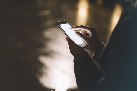 Girl pointing finger on screen smartphone on background illumination bokeh color light in night atmospheric city, hipster using in female hands and texting mobile phone, mockup glitter street, content lifestyleの写真素材