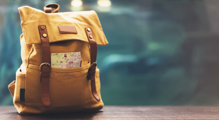 Hipster yellow backpack and map closeup. View from front tourist traveler bag on background blue sea aquarium. Person hiker visiting oceanarium museum in Barcelona on backdrop, blank blurred mockupの写真素材