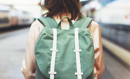Enjoying travel. Young pretty woman waiting on the station platform with backpack on background electric train. Tourist texting message and plan route of railway, railroad transport conceptの写真素材