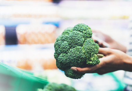 Young woman shopping healthy food in supermarket blur background. Female hands buy products broccoli using smartphone in store. Hipster at grocery using smartphone. Person comparing price of produceの写真素材
