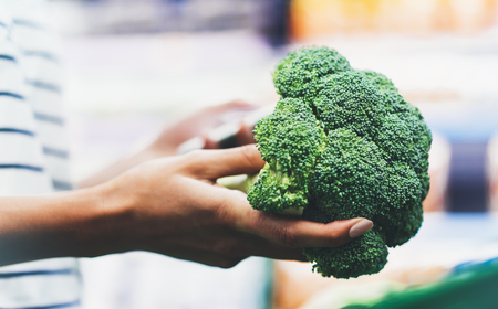 The buyer weighs the green fresh broccoli close up, woman shopping healthy food in supermarket blur background, female hands buy nature products in store groceryの写真素材