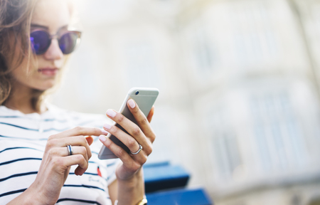 Hipster texting message on smartphone or technology, mockup of blank screen. Girl using cellphone on building castle background close. Tourist female hands holding gadget on blurred summer backdropの写真素材