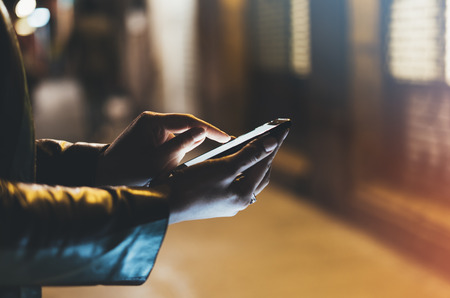 Girl pointing finger on screen smart phone on background illumination color light in night atmospheric city, hipster using in female hands and text mobile phone, mock up glitter street, content lifestyleの写真素材