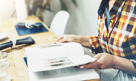 Young girl reads book during breakfast and coffee, female hands close up flipping through magazine pages in home relax atmosphere room on background of natural wooden table, woman is studying, mockの写真素材