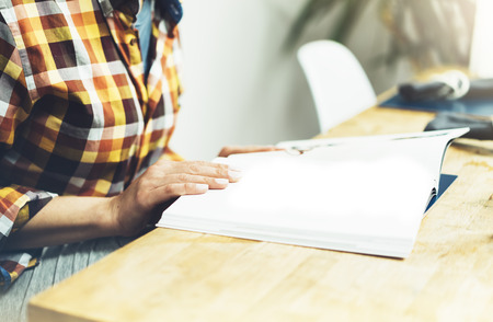 Young girl reads book during breakfast and coffee, female hands close up flipping through magazine pages in home relax atmosphere room on background of natural wooden table, woman is studying, mockの写真素材