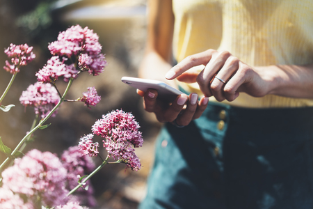 Hipster text message on smart phone or technology, mock up of blank screen. Young girl using cellphone on color flower background close. Tourist female hands holding gadget on blurred summer backdropの写真素材