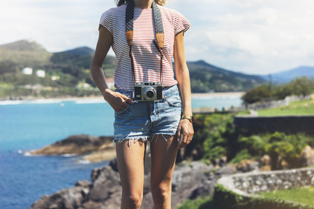 Tourist traveler photographer making pictures sea scape on vintage photo camera on background ocean, hipster girl enjoying peak mountain and nature holiday, mock up ocean waves view, blurred backdropの写真素材