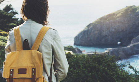 Hipster young girl with backpack enjoying sunset on seascape on peak mountain. Tourist traveler on background valley landscape view mockup. Hiker looking sunlight ocean in trip holiday in basque islandの写真素材
