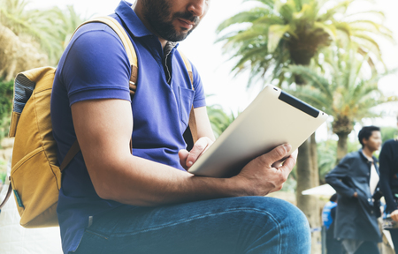 Hipster person holding in hands digital tablet with blank screen, man reading on computer on background nature park palm landscape, mock up technology blur, male hands tourist using gadget, smileの写真素材
