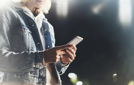 Girl pointing finger on screen smartphone on background illumination bokeh color light in night atmospheric city bridge, hipster using in female hands and texting mobile phone, mockup glitter street lifestyleの写真素材