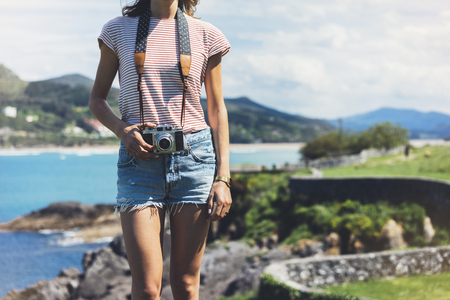 Tourist traveler photographer making pictures sea scape on vintage photo camera on background ocean, hipster girl enjoying peak mountain and nature holiday, mock up ocean waves view, blurred backdropの写真素材