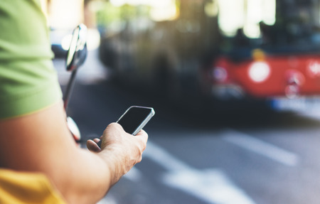Man pointing on screen smartphone on background red bus, tourist hipster waiting taxi and using in hands mobile phone, traveler connect wifi internet, headlights auto on backdrop city street, mockup stationの写真素材