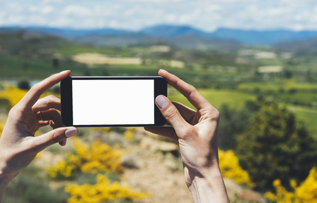 Hipster photograph on smart phone gadget mobile, mock up of blank screen. Traveler hold and using in hand mobile on background mountain landscape horizon. Tourist look map on trip, lifestyle conceptの写真素材