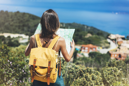 Hipster tourist hold and look map on trip, lifestyle concept adventure, traveler with backpack on background mountain and blue sea landscape horizon, young girl hiker pointing hands on trekking planの写真素材