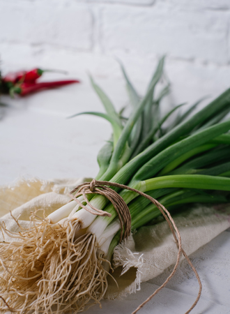 Bunch of green young scallions with roots on a white background of old wooden boards vintage top view, healthy diet food, mock up kitchen table, leek of cooking process, blur の写真素材