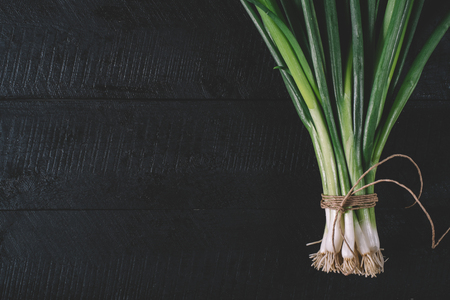 Bunch of green young scallions with roots on a black dark background of the old wooden boards vintage top view, agriculture concept, beetroot onion on cooking process on kitchen table, mock up の写真素材