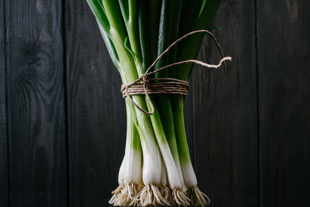 Bunch of green young scallions with roots on a black dark background of the old wooden boards vintage top view, agriculture concept, beetroot onion on cooking process on kitchen table, mock upの写真素材