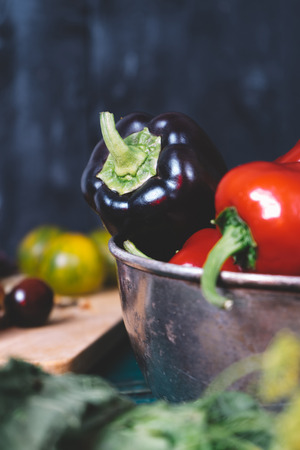 Sweet pepper in a round metal bowl and a bunch of basil in white textiles and wooden table from old vintage boards, fresh diet vegetable food on mock up background kitchen, closeup blurの写真素材
