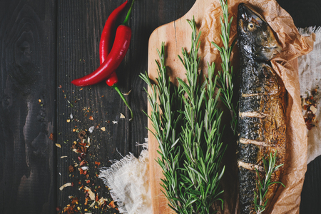 Fish with rosemary on parchment paper on a black wooden background, healthy food on kitchen table top view, grill seafood in restaurant, mackerel mediterranean of nutritionの写真素材