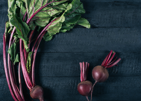 Beets with green tops in round metal pan on dark black wooden background, fresh red beetroot on backdrop kitchen table top view, healthy vitamin vegan food, organic nature plant in garden, dieting concept mock upの写真素材