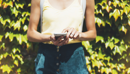Hipster text message on smart phone or technology, mock up of blank screen. Young girl using cellphone on yellow flower background close. Tourist female hands holding gadget on blurred summer backdropの写真素材