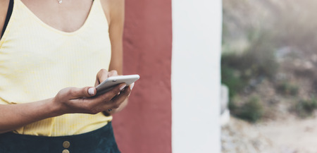 Hipster text message on smart phone or technology, mock up of blank screen. Young girl using cellphone on yellow flower background close. Tourist female hands holding gadget on blurred summer backdropの写真素材