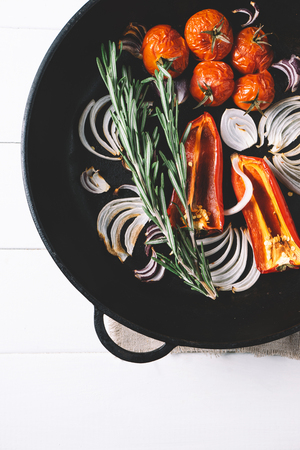 Fresh pepper and grilled cherry tomatoes, rosemary and pepper on parchment paper and cutting board on a white background of the old wooden boards vintage top view,  diet healthy vegetable food on mock up kitchen tableの写真素材