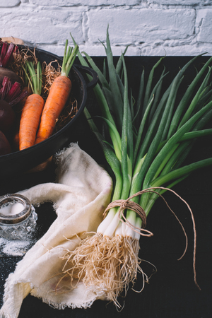 Bunch of green young scallions with roots and salt on a black dark background of the old wooden boards vintage top view, agriculture concept, beetroot onion on cooking process on kitchen table, mock up の写真素材