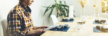 Young girl reads book during breakfast and coffee, female hands close up flipping through magazine pages in home relax atmosphere room on background of natural wooden table, woman is studying, mockの写真素材