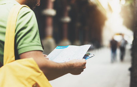 Hipster young man with backpack looking and holding map. Said view tourist traveler planning route on background sun city. Person visiting the sights Barcelona. Mockup, backdrop summer streetの写真素材