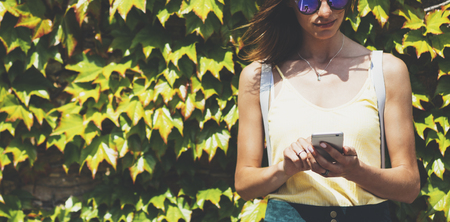 Portrait young women in sunglasses using smart phone isolated on background green nature wall mock up, pretty hipster female hands text message holding mobile gadget, blurred summer backdropの写真素材