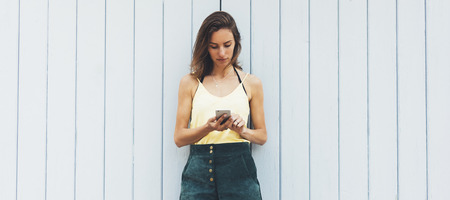 Portrait young women using smart phone isolated on background vintage wooden boards wall background mock up, pretty hipster female hands text message holding mobile gadget, blurred summer backdropの写真素材