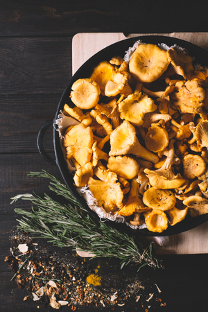 Chanterelles mushrooms in a pan with rosemary, garlic, onions, green beans and spices on a black vintage background of the old wooden boards, vegan healthy food top view and free space, mock upの写真素材