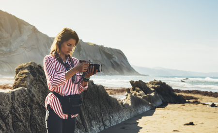 Hipster hiker tourist with backpack taking photo of amazing seascape sunset on camera on background mountains, photographer enjoying ocean horizon, blurred panoramic sunrise blank mockup, traveler relax holiday concept, sunlight view in trip vacation nortのeditorial素材