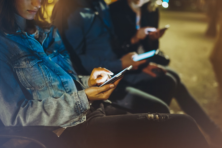 People together pointing finger on screen smartphone on background bokeh light in night atmospheric city, group adult hipsters friends using in hands modern mobile phone closeup, street online wi-fi internet conceptの写真素材