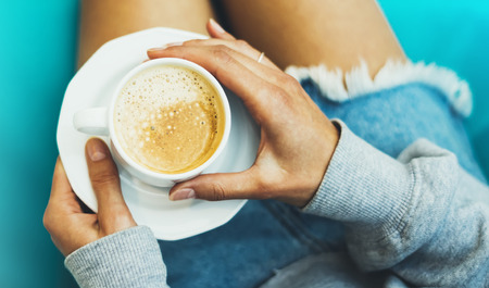 Young woman holding in female hands and drink hot aroma cup of coffee cuppuccino in breakfast time, hipster traveler girl in the morning sun day, holiday relax white cafe, top view blur, vacation atmosphere concept, closeupの写真素材