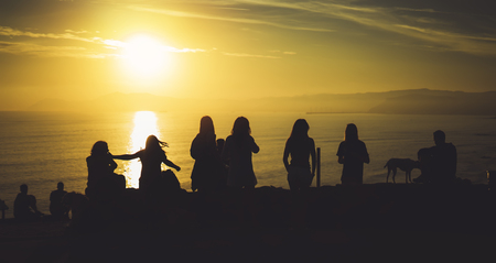 Group of young friends on background beach ocean sunrise, silhouette romantic people dances looking on rear view evening seascape, happy hipster enjoy sunset together, travel holidays vacation, love relax conceptの写真素材