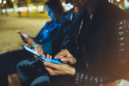 People together pointing finger on screen smartphone on background bokeh light in night atmospheric city, group adult hipsters friends using in hands modern mobile phone closeup, street online wi-fi internet conceptの写真素材